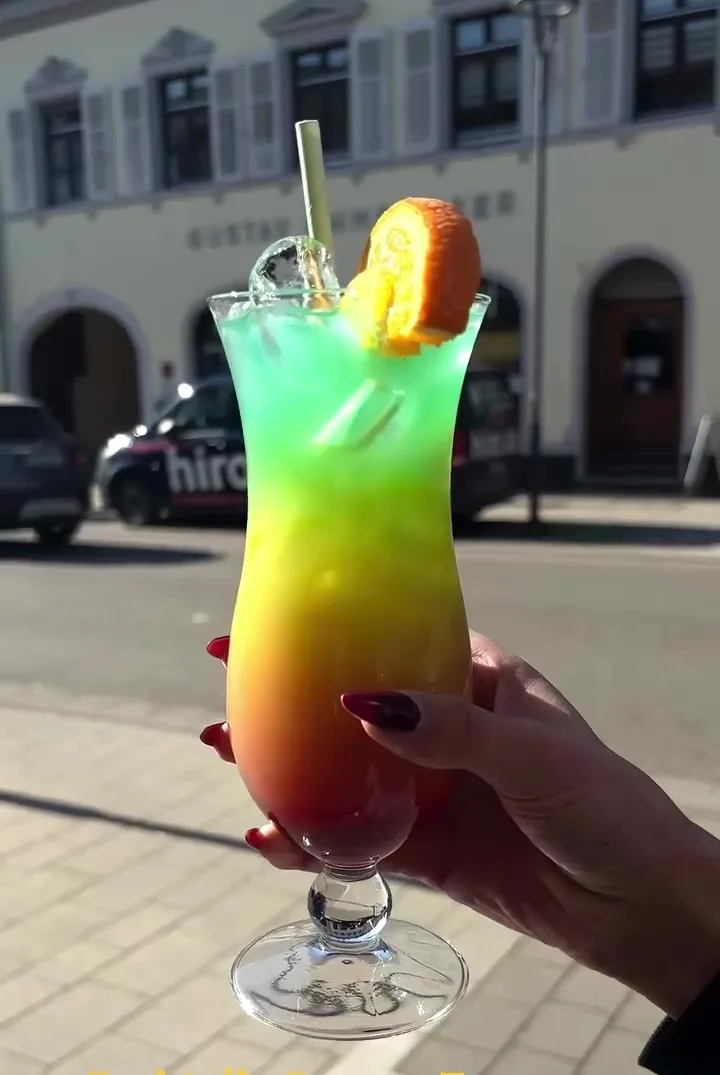 Regenbogen-Cocktail mit Orangenscheibe im Sonnenlicht